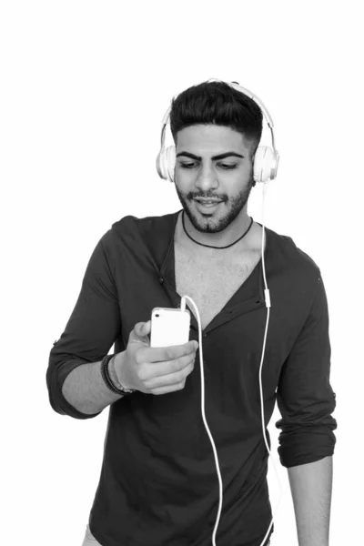 Studio shot de jeune bel homme indien utilisant un téléphone portable tout en écoutant de la musique — Photo