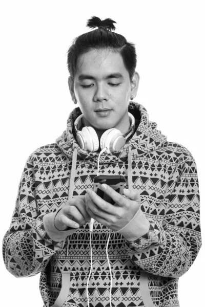 Photo prise au studio d'un jeune homme asiatique portant un casque autour du cou alors qu'il utilisait un téléphone portable — Photo