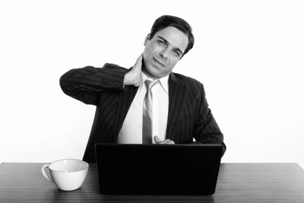 Estudio de tiro de joven empresario persa sentado mientras tiene dolor de cuello con el ordenador portátil y taza de café en la mesa de madera —  Fotos de Stock