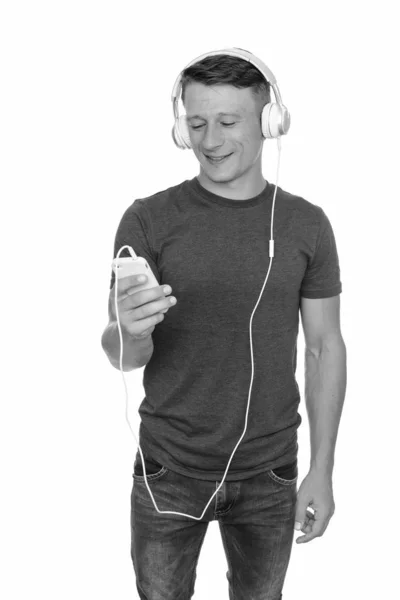 Studio shot van gelukkig Kaukasische jongeman houden van mobiele telefoon en luisteren naar muziek — Stockfoto
