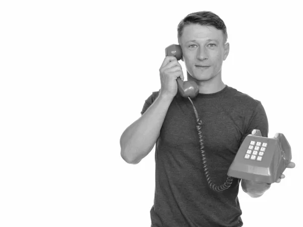 Студийный снимок молодого красивого белого мужчины, разговаривающего по старому красному телефону на белом фоне — стоковое фото