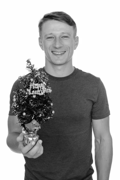 Studio shot of young handsome Caucasian man holding Happy New Year tree isolated against white background — Stock Photo, Image