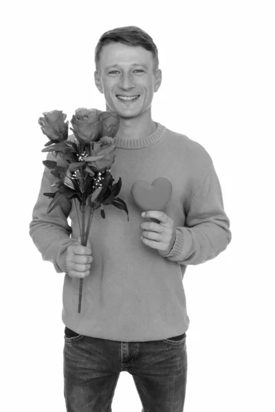 Studio ujęcie młodego, szczęśliwego białego człowieka gotowego na Walentynki z różami i czerwonym sercem — Zdjęcie stockowe