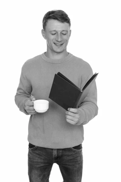 Estudio disparo de joven feliz caucásico hombre leyendo libro y sosteniendo taza de café —  Fotos de Stock