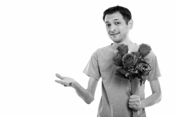 Estúdio tiro de jovem feliz sorrindo enquanto segurando rosas vermelhas e mostrando algo pronto para o dia dos namorados — Fotografia de Stock
