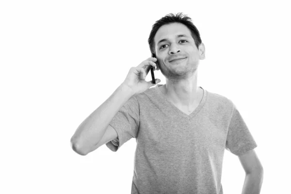 Студийный снимок счастливого молодого человека, улыбающегося и думающего во время разговора по мобильному телефону — стоковое фото