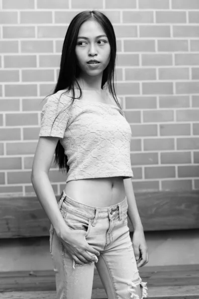 Ung Vacker asiatisk tonårsflicka ständiga samtidigt tänka och ser tillbaka mot tegelvägg — Stockfoto