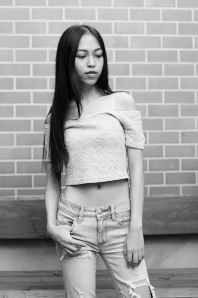 Молодих красивих азіатських Дівчинка-підліток стоячи під час мислення і, дивлячись проти цегляна стіна — стокове фото