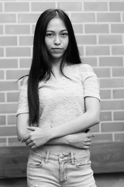 Young beautiful Asian teenage girl with arms crossed against brick wall — Stock Photo, Image