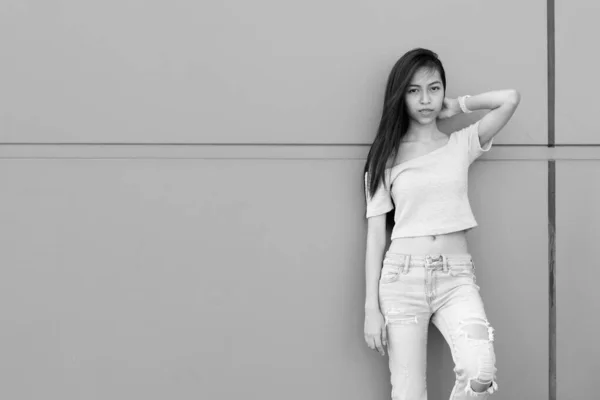 Young beautiful Asian teenage girl holding her hair while leaning against concrete wall outdoors — Stock Photo, Image