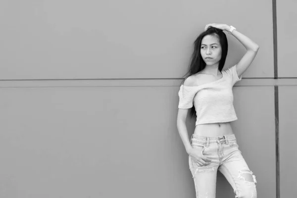 Jeune belle adolescente asiatique penser avec la main sur la tête tout en se penchant contre le mur de béton à l'extérieur — Photo