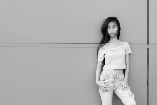 Jeune belle adolescente asiatique penser et regarder la distance tout en se penchant contre le mur de béton à l'extérieur — Photo