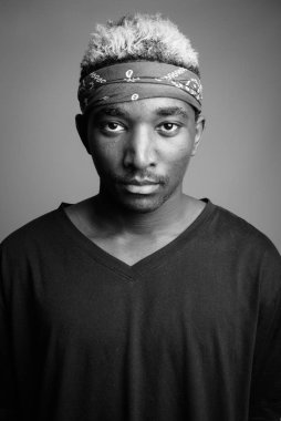 Gri arka planda saç bandı olarak bandana takan genç bir Afrikalı.