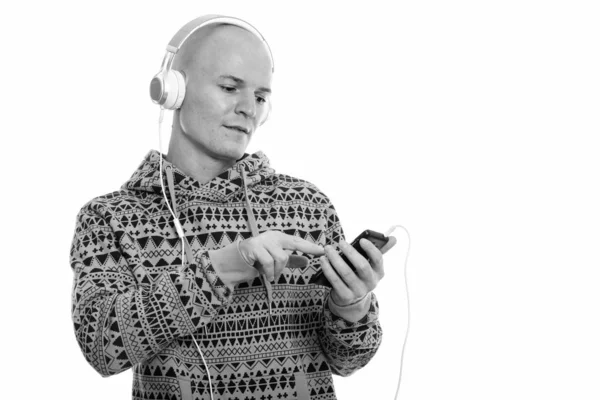 Studio shot of young handsome bald man using mobile phone while listening to music — Stock Photo, Image