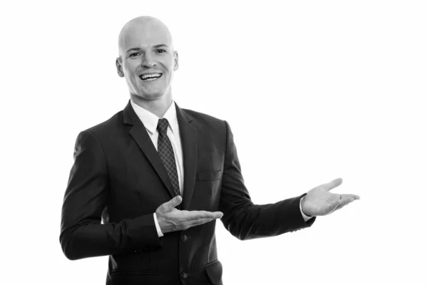 Estúdio tiro de jovem feliz homem de negócios careca sorrindo ao mostrar algo — Fotografia de Stock