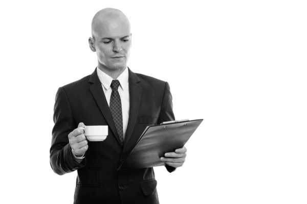 Estudio de disparo de joven hombre de negocios calvo guapo leyendo en el portapapeles mientras sostiene la taza de café — Foto de Stock