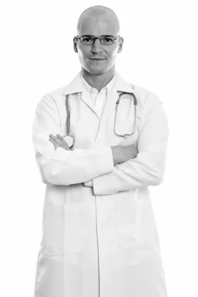 Studio shot de jeune homme chauve beau médecin debout et portant des lunettes avec les bras croisés — Photo