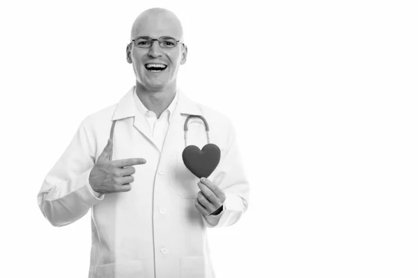 Joven hombre calvo feliz médico sonriendo mientras sostiene y señala el corazón rojo —  Fotos de Stock