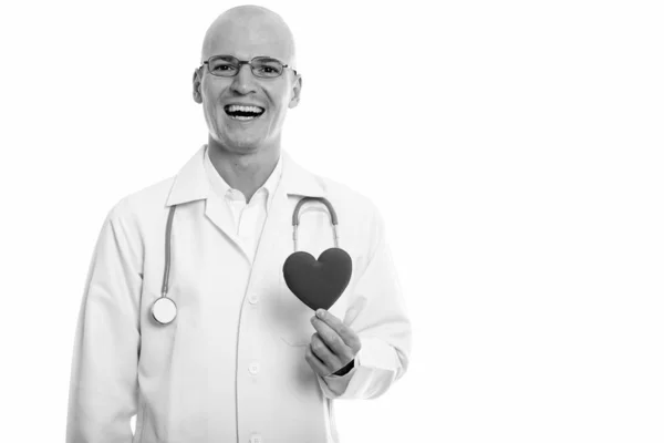 Estudio de tiro de joven hombre calvo feliz médico sonriendo mientras sostiene el corazón rojo —  Fotos de Stock