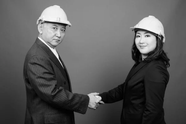 Mature Asian businessman and mature Asian businesswoman wearing hardhat together — ストック写真