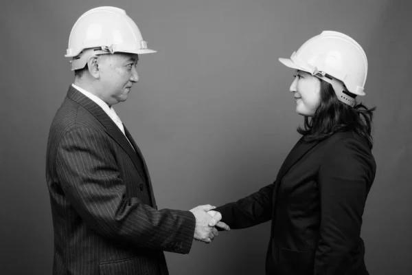 Mature Asian businessman and mature Asian businesswoman wearing hardhat together — ストック写真