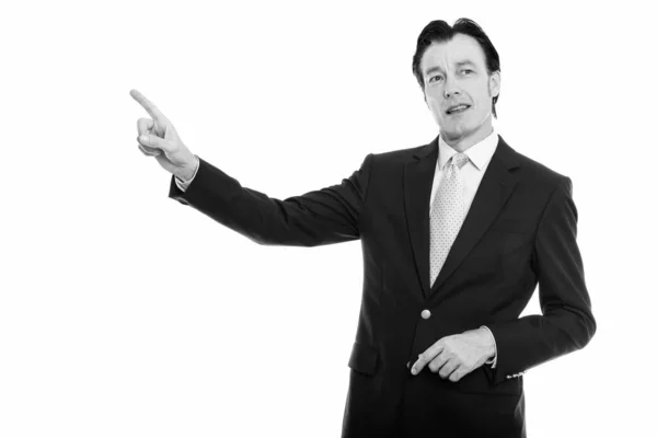 Studio shot of mature handsome businessman pointing finger while looking at distance — Stock Photo, Image