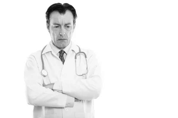 Studio shot of mature handsome man doctor thinking while looking down with arms crossed — Stock Photo, Image