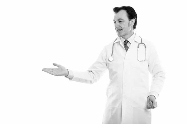 Студійний знімок зрілого щасливого лікаря, який посміхається і показує щось — стокове фото