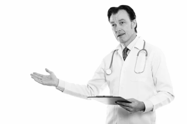 Studioaufnahme von reifem, gutaussehendem Mann Arzt hält Klemmbrett und zeigt etwas — Stockfoto