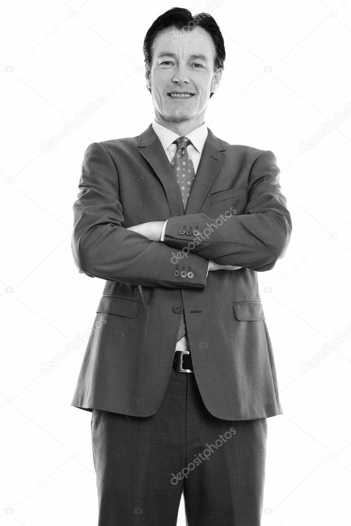 Studio shot of mature happy businessman smiling and standing with arms crossed