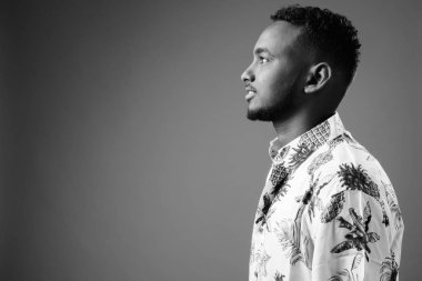 Studio shot of young handsome African tourist man ready for vacation against gray background in black and white
