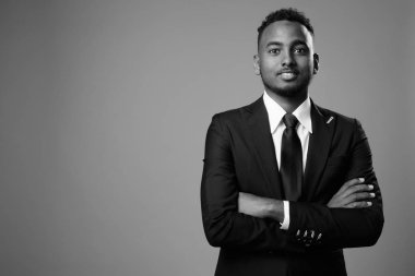 Siyah-beyaz gri arka planda takım elbiseli Afrikalı genç iş adamının stüdyo fotoğrafı.