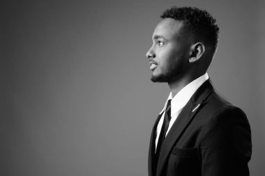 Siyah-beyaz gri arka planda takım elbiseli Afrikalı genç iş adamının stüdyo fotoğrafı.