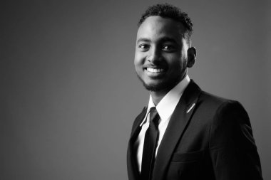 Siyah-beyaz gri arka planda takım elbiseli Afrikalı genç iş adamının stüdyo fotoğrafı.