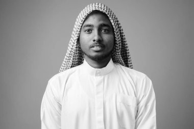 Studio shot of young handsome African man wearing traditional Muslim clothes against gray background in black and white