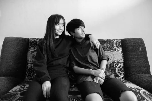 若いですアジアのレズビアンカップル座っています上のソファ一緒にと愛に家で黒と白 — ストック写真