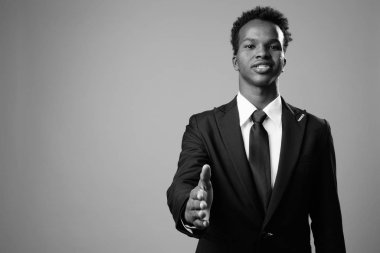 Studio shot of young African businessman against gray background in black and white