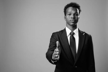 Studio shot of young African businessman against gray background in black and white