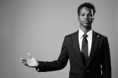 Studio shot of young African businessman against gray background in black and white