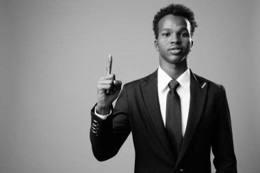Studio shot of young African businessman against gray background in black and white