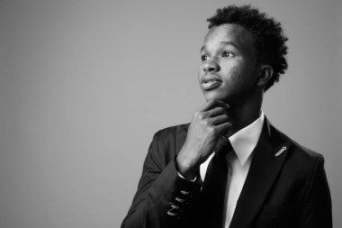 Studio shot of young African businessman against gray background in black and white