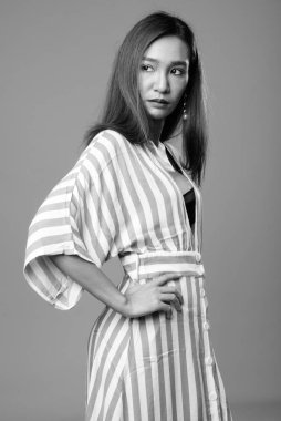 Studio shot of young beautiful slim Asian woman against gray background in black and white