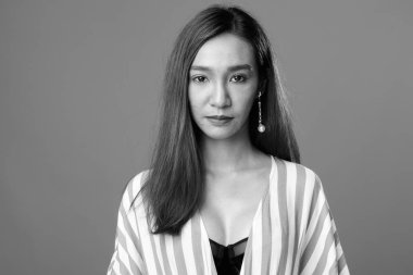 Studio shot of young beautiful slim Asian woman against gray background in black and white