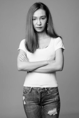 Studio shot of young beautiful slim Asian woman against gray background in black and white