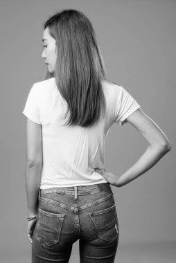 Studio shot of young beautiful slim Asian woman against gray background in black and white