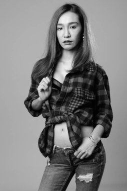 Studio shot of young beautiful Asian hipster woman against gray background in black and white