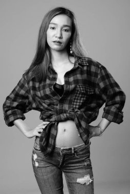 Studio shot of young beautiful Asian hipster woman against gray background in black and white