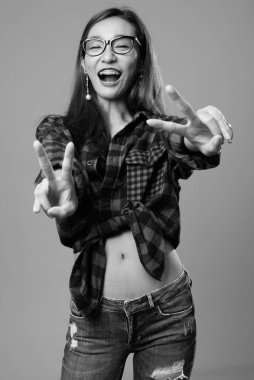 Studio shot of young beautiful Asian hipster woman against gray background in black and white