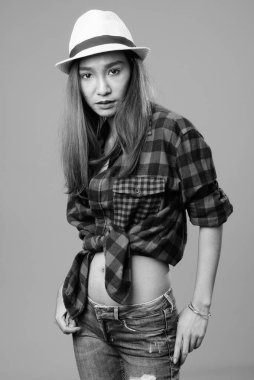 Studio shot of young beautiful Asian hipster woman against gray background in black and white
