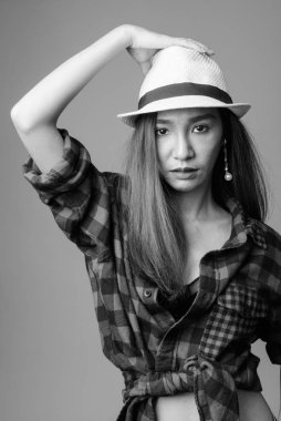 Studio shot of young beautiful Asian hipster woman against gray background in black and white